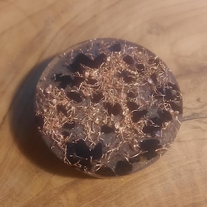 May include: A round, black and copper-colored resin orb with a swirling pattern. The orb is made of resin and has a smooth, polished finish.