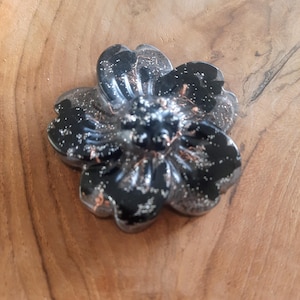 May include: A black flower-shaped resin paperweight with silver glitter embedded in the resin.