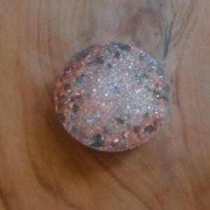 May include: A round, decorative object with a black, white, and pink glitter finish. The object has a textured surface and appears to be made of resin.