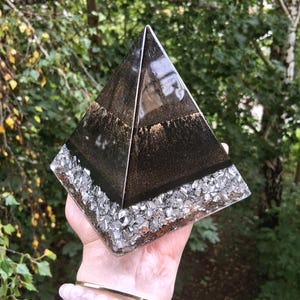 May include: A pyramid-shaped object made of resin with a smooth, glossy black top section featuring subtle gold glitter accents. The base of the pyramid is filled with a layer of jagged, reflective silver-colored metallic shards and fragments.