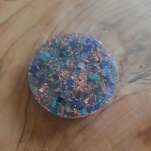 May include: A round, flat, resin-based coaster with a mix of blue, green, and gold glitter embedded in the resin. The coaster is approximately 2 inches in diameter.