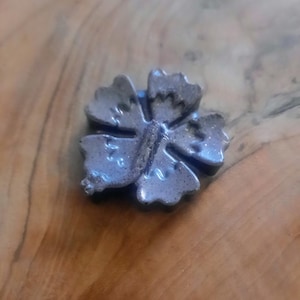 May include: A dark gray ceramic flower charm in the shape of a hibiscus. The charm has a detailed design and a glossy finish.