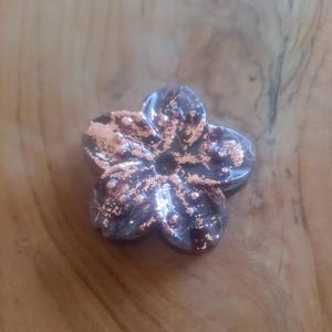 May include: A copper-colored ceramic flower with a five-petal design. The flower has a textured surface and a metallic sheen.
