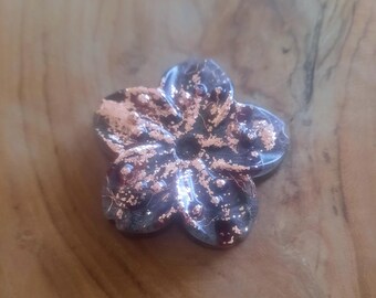 Può includere: Un fiore in ceramica color rame con un design a cinque petali. Il fiore ha una superficie testurizzata e una lucentezza metallica.