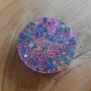May include: A round, pink, purple, and blue resin coaster with embedded crystals and gold flakes.