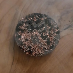 May include: A round black coaster with a copper and black design. The coaster has a textured surface and is perfect for protecting surfaces from heat and scratches.