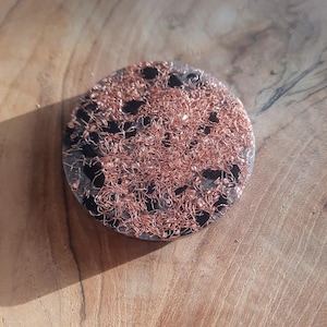 May include: A round, black and copper resin coaster with a unique, textured surface. The coaster is made with copper wire embedded in the resin.
