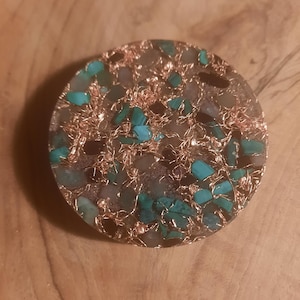 May include: A round, circular resin coaster with a copper wire design and embedded turquoise and other stones.