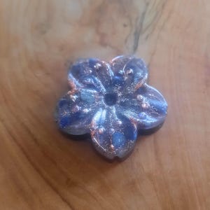 May include: A blue and silver flower-shaped resin incense burner with a hole in the center. The burner is decorated with small blue and silver glitter.