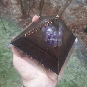May include: A clear pyramid-shaped resin sculpture with a purple amethyst crystal embedded inside. The pyramid is accented with a copper wire coil around the top edge.