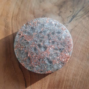 May include: A round, clear resin coaster with a silver and copper glitter embedded inside. The coaster has a unique, marbled appearance.