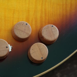 Peut inclure: Gros plan sur quatre boutons en bois avec des flèches noires sur une guitare. Les boutons sont sur un corps de guitare brun et noir.