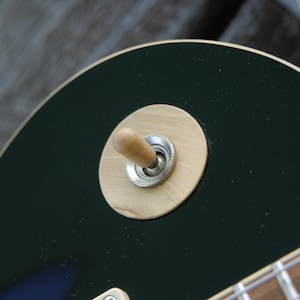 Puede incluir: Primer plano de una guitarra eléctrica negra con un interruptor de palanca de madera en una placa de arce.