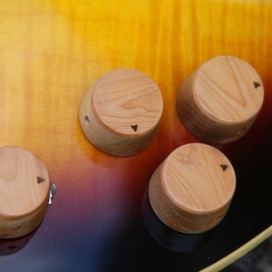 May include: Close-up of five wooden knobs with black markings on a guitar. The knobs are arranged in a semi-circle on a brown and yellow guitar body.