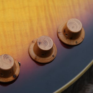 May include: Close-up of a guitar with three wooden knobs. The knobs are round and have a light brown colour. The guitar is a sunburst finish with a dark brown body.