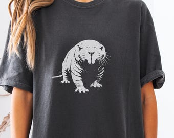 Può includere: T-shirt grigio scuro con un'illustrazione bianca di un animale simile a un roditore. La grafica è centrata sulla maglietta e raffigura l'animale di fronte. La maglietta ha maniche corte e una vestibilità ampia.