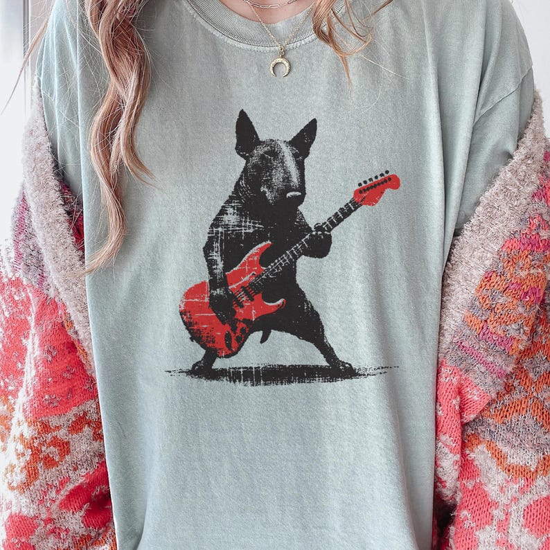 K&ouml;nnte beinhalten: Hellblaues T-Shirt mit einer schwarzen Illustration eines Bullterriers, der eine rote E-Gitarre spielt. Der Hund steht mit gespreizten Beinen. Die Gitarre hat einen Used-Look.