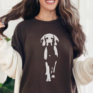 Op de afbeelding: Donkerbruin T-shirt met een witte afbeelding van een hond. De hond is afgebeeld in een eenvoudige stijl. Het T-shirt maakt deel uit van een collectie vrijetijdskleding.