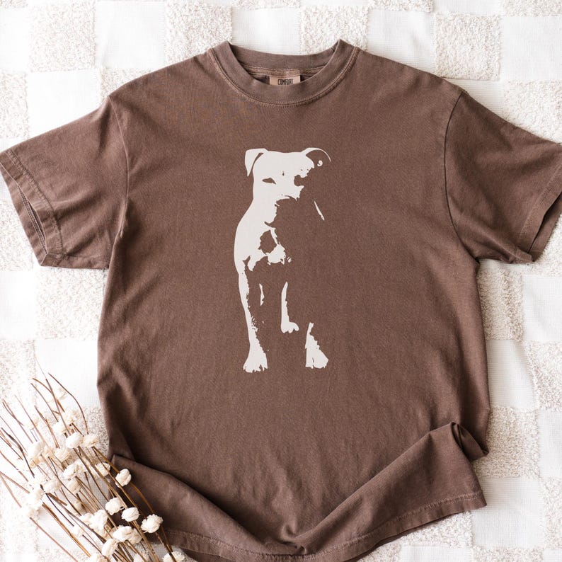 Pode incluir: Camiseta marrom com uma silhueta branca de cachorro. A camiseta tem gola redonda e mangas curtas. O desenho do cachorro est&aacute; centralizado na frente.