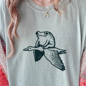 Seltsames Frosch- und Gans-Shirt - schrulliges Tier-wunderliches Geschenk-T-Stück - Kröten-Reitgans-T - Lustiges Tier-T-Shirt - Meme-T-Stück Bay