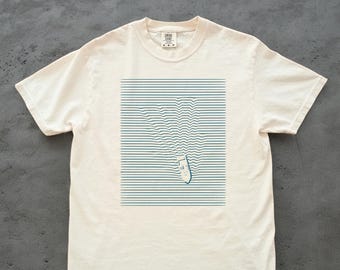 Könnte beinhalten: Cremefarbenes T-Shirt mit blau-weißem Grafikdesign. Das Design zeigt eine Bootsform mit aufsteigenden Wellenlinien, vor einem Hintergrund aus horizontalen Linien. Das T-Shirt hat kurze Ärmel und einen Rundhalsausschnitt.