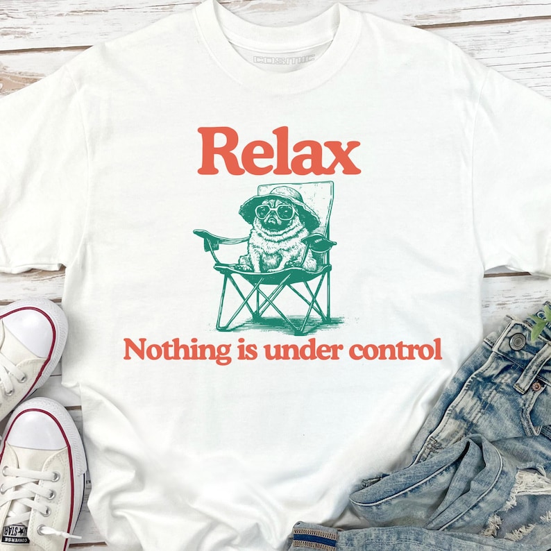 May include: White t-shirt featuring a pug wearing sunglasses and a hat, seated in a green folding chair. The text "Relax" and "Nothing is under control" are in orange.