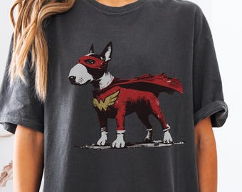 May include: Dark grey t-shirt featuring a superhero dog illustration. The dog is a Bull Terrier wearing a red cape and mask, with a gold emblem. The graphic is distressed, giving a vintage look.