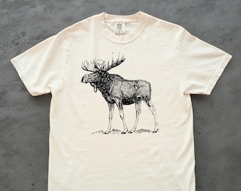以下が含まれることがあります： クリーム色のTシャツ。黒と白で描かれた、詳細なヘラジカのイラストが特徴です。 ヘラジカは立っている姿で、大きな角を見せています。 このシャツは柔らかい素材で作られています。