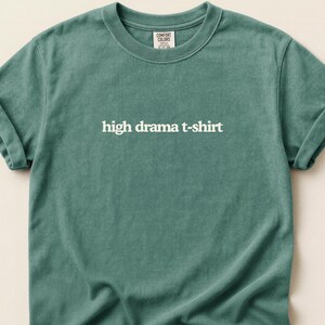 Può includere: Una tazza di ceramica bianca con manico nero e la scritta "But First, Coffee" in nero, con un carattere a mano. La tazza è su una superficie bianca.