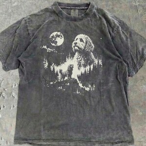 May include: A charcoal grey short-sleeve t-shirt with a mineral wash finish. The centre graphic features a white illustration of a dog standing on a rocky cliff in a forest, a large dog head in the sky, and a full moon against a dark background.