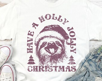 May include: A white short-sleeve t-shirt featuring a distressed purple graphic of a sloth wearing a Santa hat. The text reads HAVE A HOLLY JOLLY CHRISTMAS, framed by two small pine tree icons. The design is centered on the chest of the shirt.