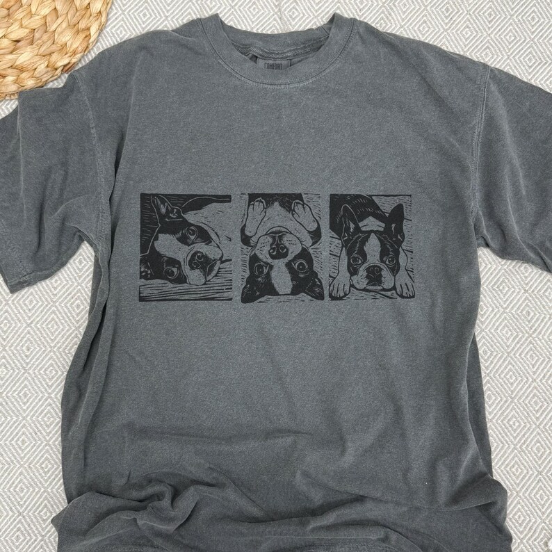 May include: Gray t-shirt featuring a black and white graphic of a Boston Terrier in three different poses. The dog is shown lying down, upside down, and looking forward. The shirt is made of a soft material.