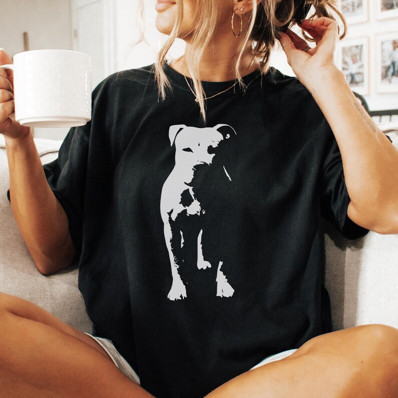 Pode incluir: Camiseta preta com um gr&aacute;fico branco de um cachorro. O cachorro &eacute; retratado em um estilo minimalista. A camiseta tem um ajuste folgado e grande. A imagem mostra um estilo casual.