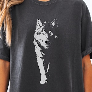 May include: Charcoal grey t-shirt with a white wolf graphic. The wolf is illustrated in a detailed, artistic style, with emphasis on its face and front legs. The shirt has short sleeves and a relaxed fit.