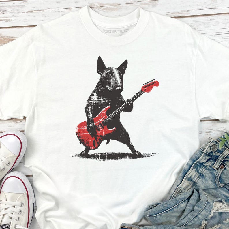 K&ouml;nnte beinhalten: Wei&szlig;es T-Shirt mit einer schwarzen Grafik eines Bullterriers, der eine rote E-Gitarre spielt. Der Hund ist in einer dynamischen Pose dargestellt und h&auml;lt die Gitarre. Das T-Shirt wird mit Jeans und wei&szlig;en Turnschuhen kombiniert.