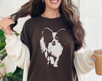 Puede incluir: Camiseta marrón oscuro con un gráfico blanco de un perro Papillon. El perro está representado en una ilustración detallada y estilizada. La camiseta es de estilo casual, adecuada para el uso diario.