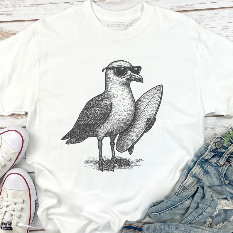 K&ouml;nnte beinhalten: Ein wei&szlig;es T-Shirt mit einer schwarz-wei&szlig;en Strichzeichnung einer M&ouml;we, die eine Sonnenbrille tr&auml;gt und ein Surfbrett unter dem Fl&uuml;gel h&auml;lt. Die Grafik ist mittig auf der Brust platziert und zeigt detaillierte Federstrukturen und Schattierungen.