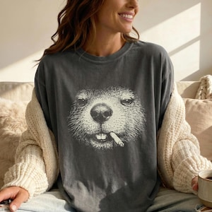 Könnte beinhalten: Dunkelgraues T-Shirt mit einer detaillierten Illustration eines Murmeltiers mit einer Zigarette im Mund. Das Gesicht des Murmeltiers ist im Vintage-Stil gehalten. Das Shirt hat eine lockere Passform und einen Rundhalsausschnitt.