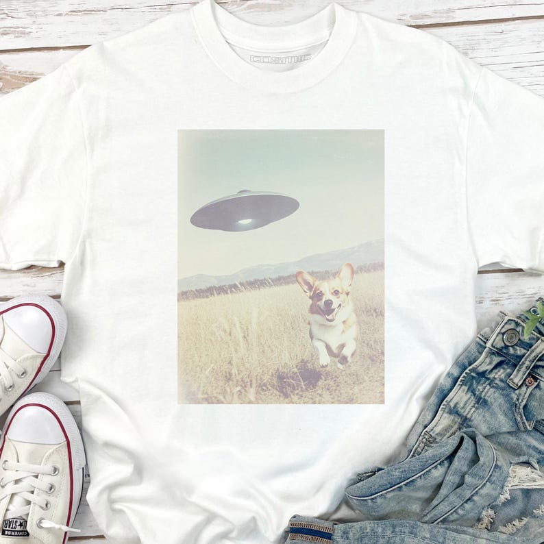 May include: White t-shirt with a graphic of a corgi running towards a UFO in a field. The graphic is in a vintage style.