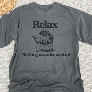 May include: Grey t-shirt featuring the word "Relax" above a pug illustration in a chair and hat. The text "Nothing is under control" is printed below the illustration.