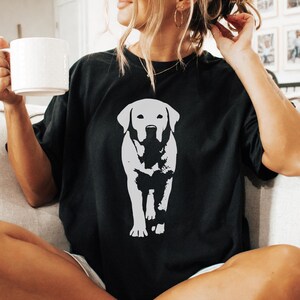 May include: Black t-shirt featuring a white graphic of a Labrador Retriever. The dog is depicted in a standing pose, with detailed features. The shirt is a casual style, suitable for everyday wear.