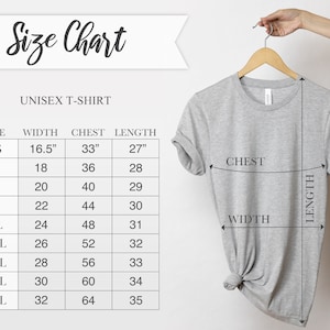 Puede incluir: Una camiseta unisex gris colgada de una percha de madera, con una tabla de tallas a la izquierda. La tabla detalla las medidas de ancho, pecho y largo en cent&iacute;metros para las tallas XS a 5XL. El texto "Size Chart" est&aacute; en la parte superior.