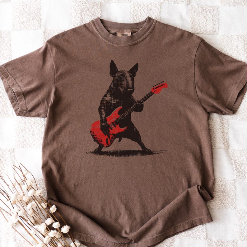 K&ouml;nnte beinhalten: Braunes T-Shirt mit einem schwarzen Hund, der eine rote E-Gitarre spielt. Der Hund steht mit gespreizten Beinen und h&auml;lt die Gitarre. Das Shirt hat einen Rundhalsausschnitt und kurze &Auml;rmel. Das Design ist grafisch.