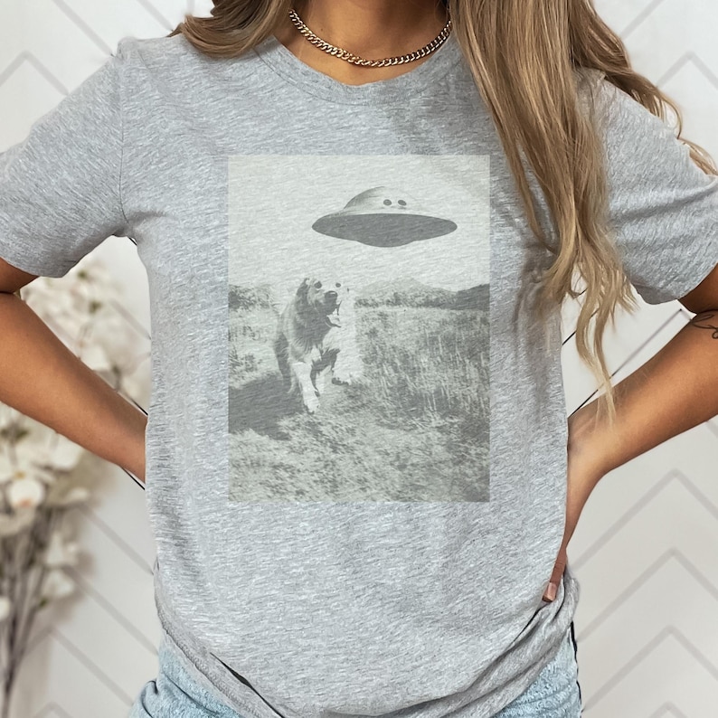 May include: A gray t-shirt with a black and white image of a dog looking up at a flying saucer.