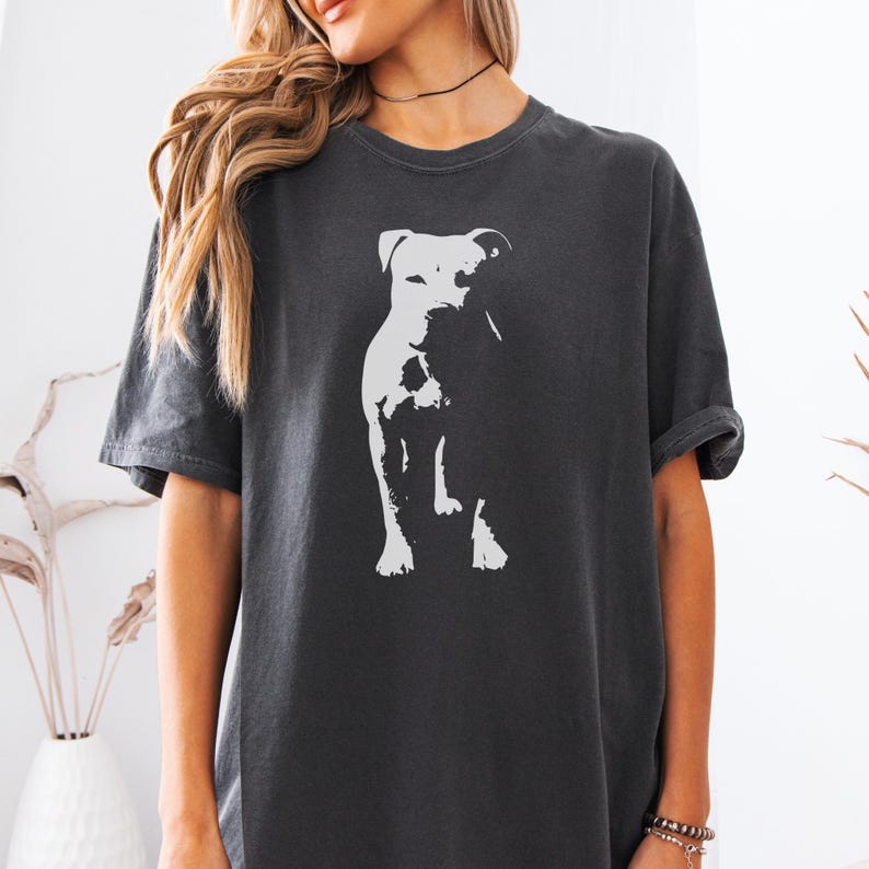Pode incluir: T-shirt cinzenta escura com um gr&aacute;fico branco de um c&atilde;o. O c&atilde;o &eacute; retratado num estilo minimalista. A camisola tem mangas curtas e um ajuste descontra&iacute;do. O design &eacute; simples e casual, adequado para o uso di&aacute;rio.