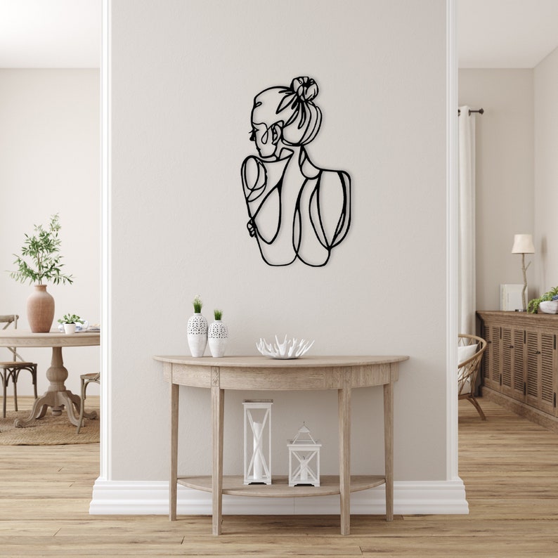 May include: Black metal wall art depicting a stylized outline of a person with their hair pulled back in a bun.