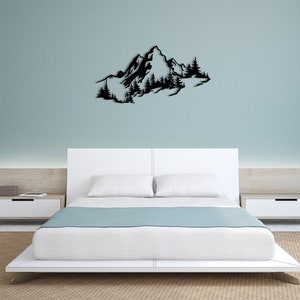 May include: Black metal wall art depicting a mountain range with trees. The art is mounted on a white wall above a white bed with a light blue blanket.