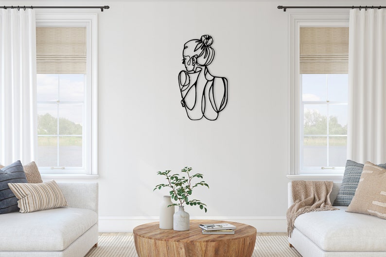 May include: Black metal wall art sculpture of a woman with her hair in a bun. The sculpture is in a minimalist style and is a modern home decor piece.