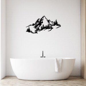 May include: Black metal wall art depicting a mountain range with trees. The art is mounted on a white wall above a white bathtub.