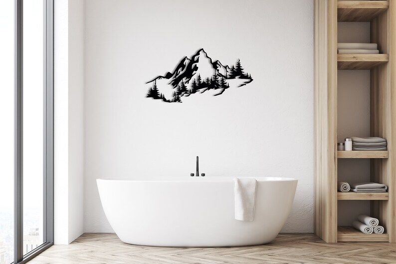 May include: Black metal wall art depicting a mountain range with trees. The art is mounted on a white wall above a white bathtub.